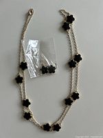 Necklace with multiple black flower stations and bagged matching earrings displayed on surface