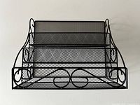 Front view of black metal mesh three-tier letter organizer showing structure and decorative scrollwork