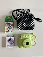Front view of lime green instant camera, polka-dot case and two film boxes