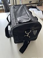 Three-quarter view of black soft pet carrier showing mesh end, shoulder strap, top zip flap