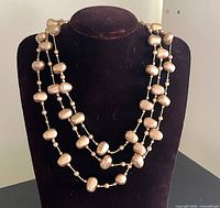 Full view of the triple strand beige-gold faux pearl necklace on display bust