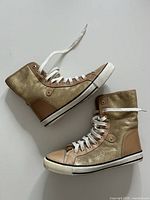 Side view of both sneakers showing gold glitter panels, tan leather trim, white rubber soles