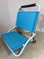 Left-front view of blue folding beach chair showing seat fabric, white frame and foam handle