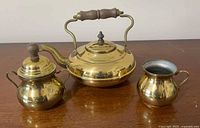 Front view of complete 3-piece brass tea set showing teapot, sugar bowl, and creamer