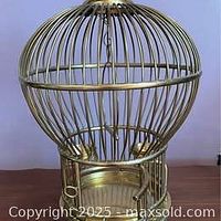 Front view of brass bird cage showing dome top and base.