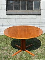 Full view of round teak dining table on four-star pedestal base outdoors