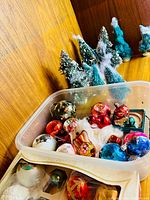 Plastic tub with mixed glass ornaments and background bottle brush trees
