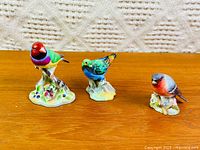 Three porcelain bird figurines on wood surface