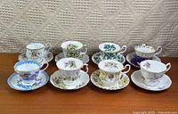 Eight cup and saucer sets displayed on wooden surface