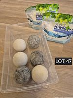 Six wool dryer balls in clear bin with two Norwex Ultra Power Plus detergent pouches