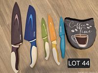 Five colour-coded kitchen knives with guards and Coffee Time oven mitt on wood floor