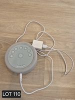 White noise machine with attached cable and AC adapter on wooden surface