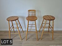 Front view of three wood bar stools, showing one with backrest and two without