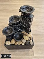 Front view of black speckled resin multi-tier fountain with river stones in square base