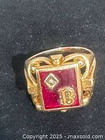 Front view of ring showing ruby-colored stone, diamond accent, monogram B, and gold setting