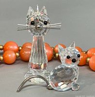 Front view of both Swarovski crystal cat figurines with bead necklace backdrop