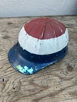 Oblique view of aluminum hard hat showing red crown, white band, blue brim, paint chipping