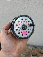 Front view of fly reel showing perforated spool, center knob marked "OSS 275"