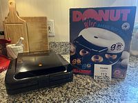 Closed black Salton waffle maker next to boxed Maxim donut maker