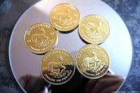 Five gold-tone 1967 Krugerrand copy coins on reflective surface