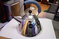Side view of kettle displaying polished body, blue handle, bird whistle and Alessi badge