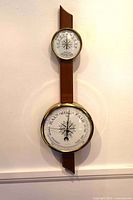 Full view of wall-mounted dual-dial barometer on teak backboard