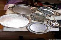 Overview of six visible silver-plated pieces including round trays, bread tray, gravy boat with underplate