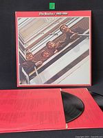 Front of gatefold jacket shown upright with one vinyl disc partially visible in red inner sleeve