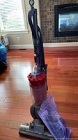 Full view of Dyson DC41 Ball upright vacuum standing on hardwood floor with purple bag holding attachments
