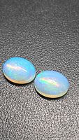 Pair of oval cabochon opals on dark background showing play-of-colour