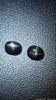 Two oval black star diopside cabochons on textured surface