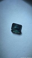 Emerald-cut blue-green sapphire on neutral surface