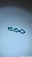 Three oval-cut blue zircons on neutral background