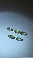 Five oval green sapphires arranged on neutral background