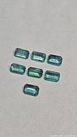 Eight rectangular emerald-cut green gemstones on neutral background