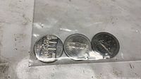 Three coins in plastic sleeve reverse sides visible
