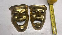 Front view of both brass masks with measuring tape for scale