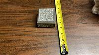 Closed pewter box beside tape measure showing size