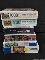 Stack of six sealed puzzle boxes showing brands and piece counts