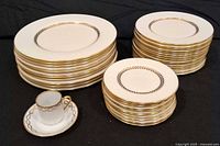 Stacks of dinner, salad and bread plates with gold trim and one teacup with saucer in foreground