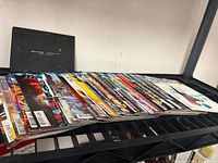 Stack of DC Rebirth comics and black art folio on shelf