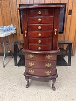 Full view of closed wooden jewelry armoire showing drawers and cabriole legs