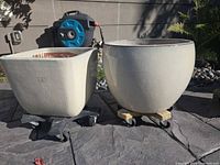 Two round and one square beige glazed ceramic plant pots on caster bases