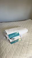 Folded king silk duvet with product leaflet on top of quilted mattress pad