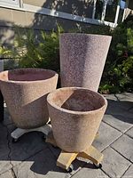 Three brown speckled planters on patio, two sizes visible with caddies