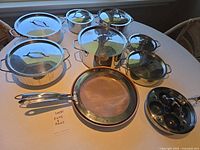Group view of seven stainless pots with lids, copper-bottom pan and egg poacher pan