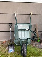 Front view of TUFX wheelbarrow standing upright beside Garant shovel