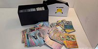 Open black storage box full of Pokémon cards, white Celebrations insert and spread of assorted cards on table