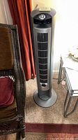Full view of gray Lasko tower fan standing on round base