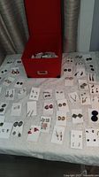 Overview of many earring pairs laid out on table with red storage box